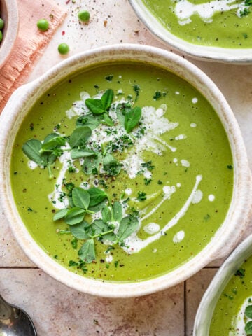 Overhead view of broccoli and pea soup with a cream and herb garnish.