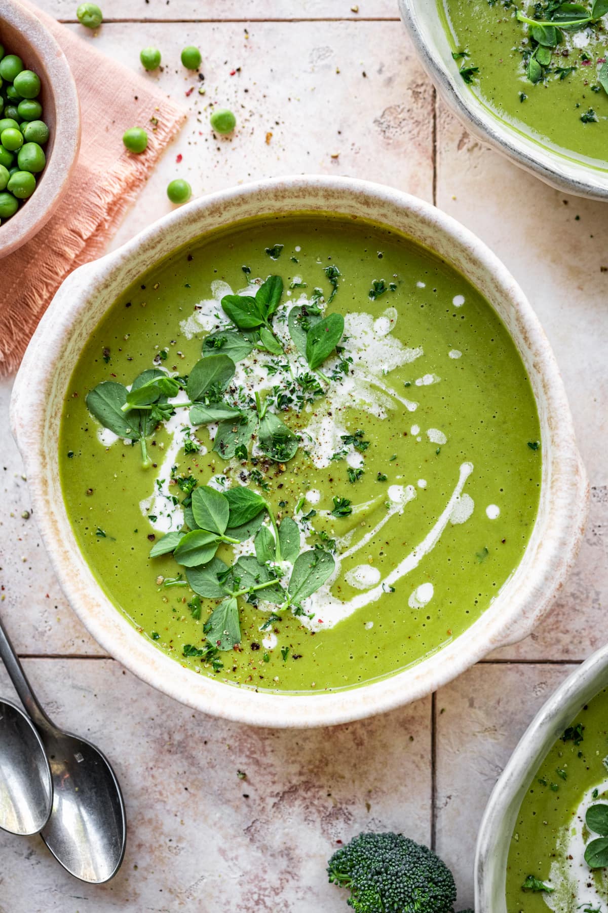 Overhead view of broccoli and pea soup with a fresh herb and cream garnish.