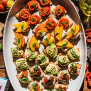 overhead view of 4 varieties of crackers with toppings on white platter.