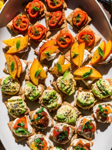 overhead view of 4 varieties of crackers with toppings on white platter.