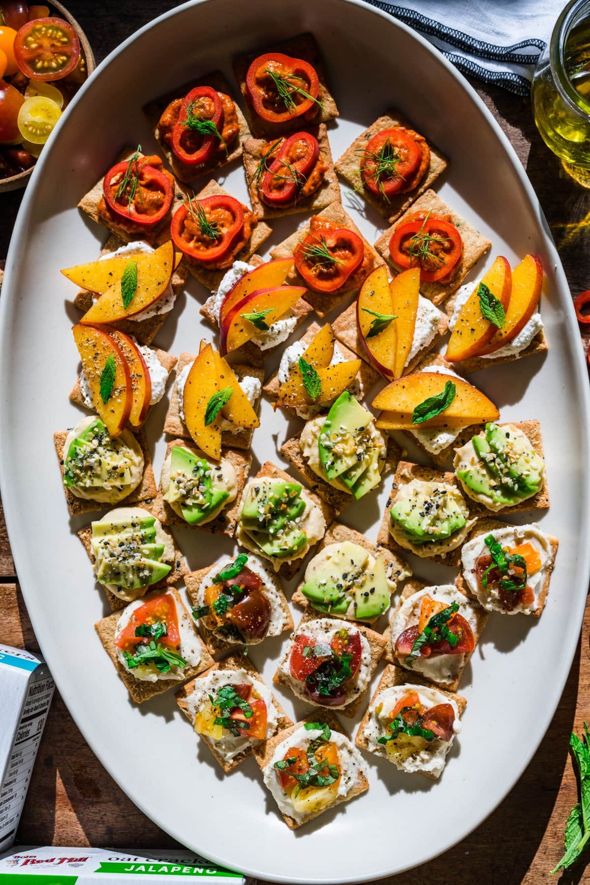 overhead view of 4 varieties of crackers with toppings on white platter. 