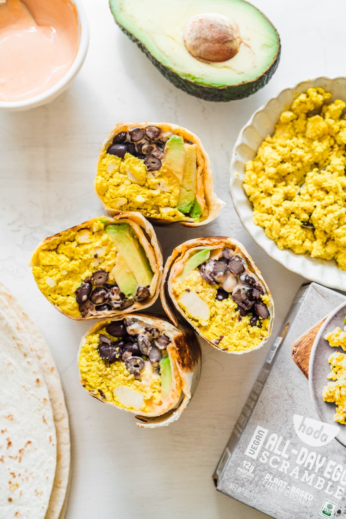 overhead view of several breakfast burritos cut in half on white backdrop. 