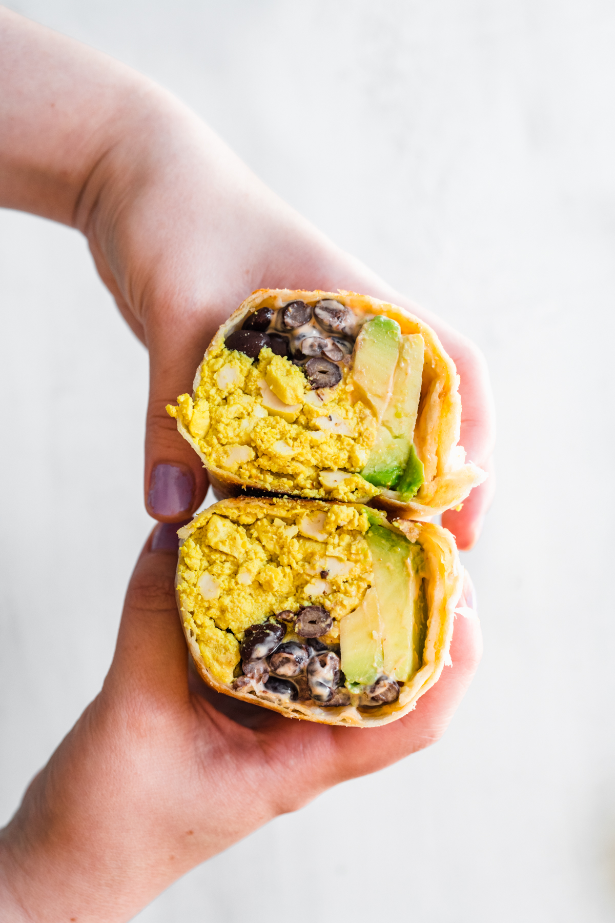 close up of person holding vegan breakfast burrito cut in half. 