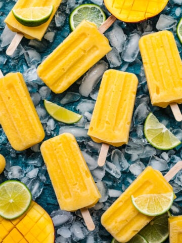 Overhead view of mango popsicles on a blue background.