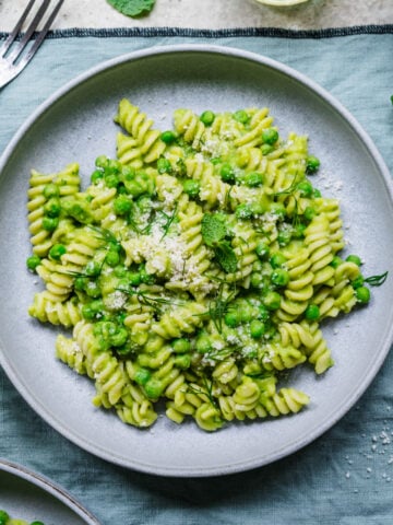 Overhead of finished pasta with pea sauce in bowl on green linen.