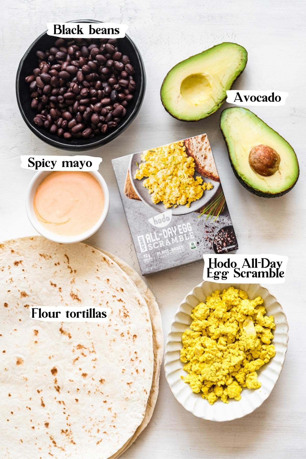 overhead view of ingredients for vegan breakfast burrito, including avocado, black beans, tortillas, mayo and tofu scramble. 