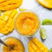 Finished mango jam in mason jar with mangos on the side.