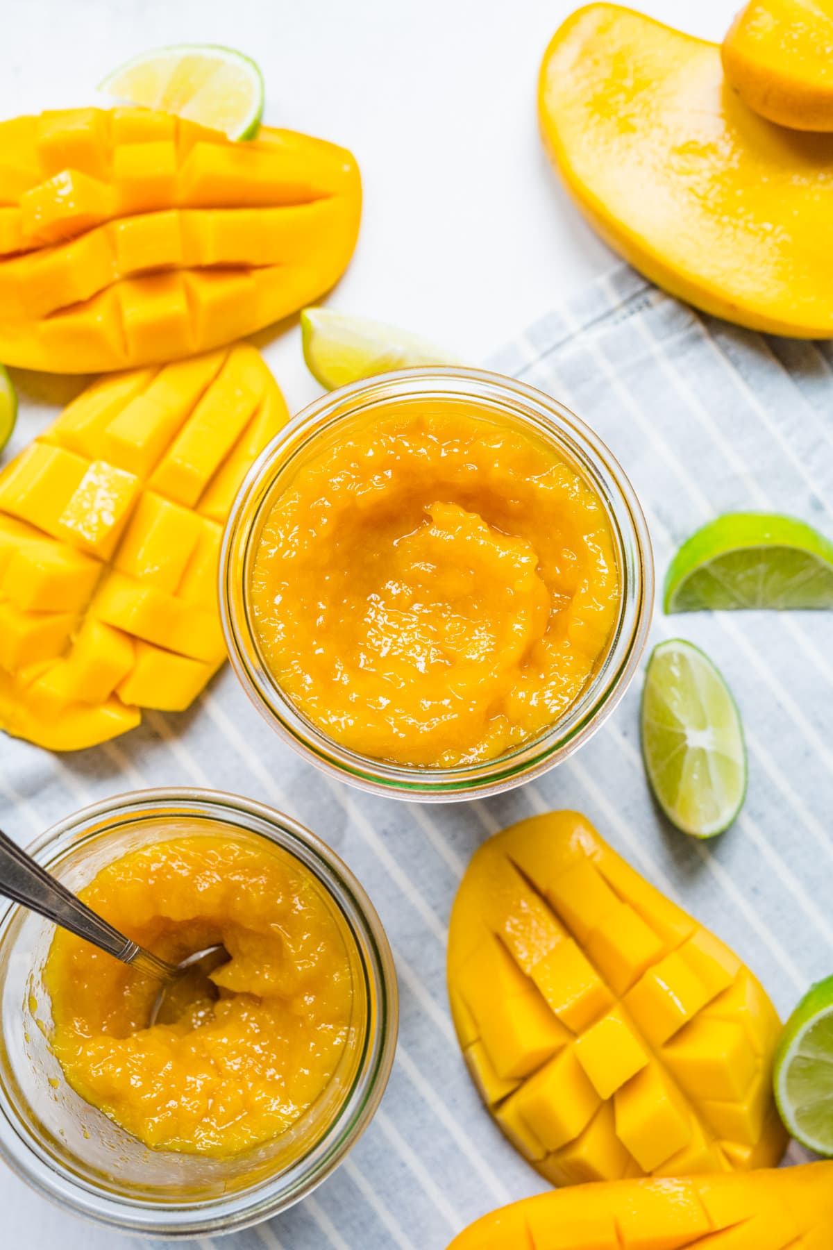 Finished mango jam in mason jar with mangos on the side.