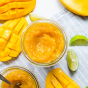 Finished mango jam in mason jar with mangos in background.