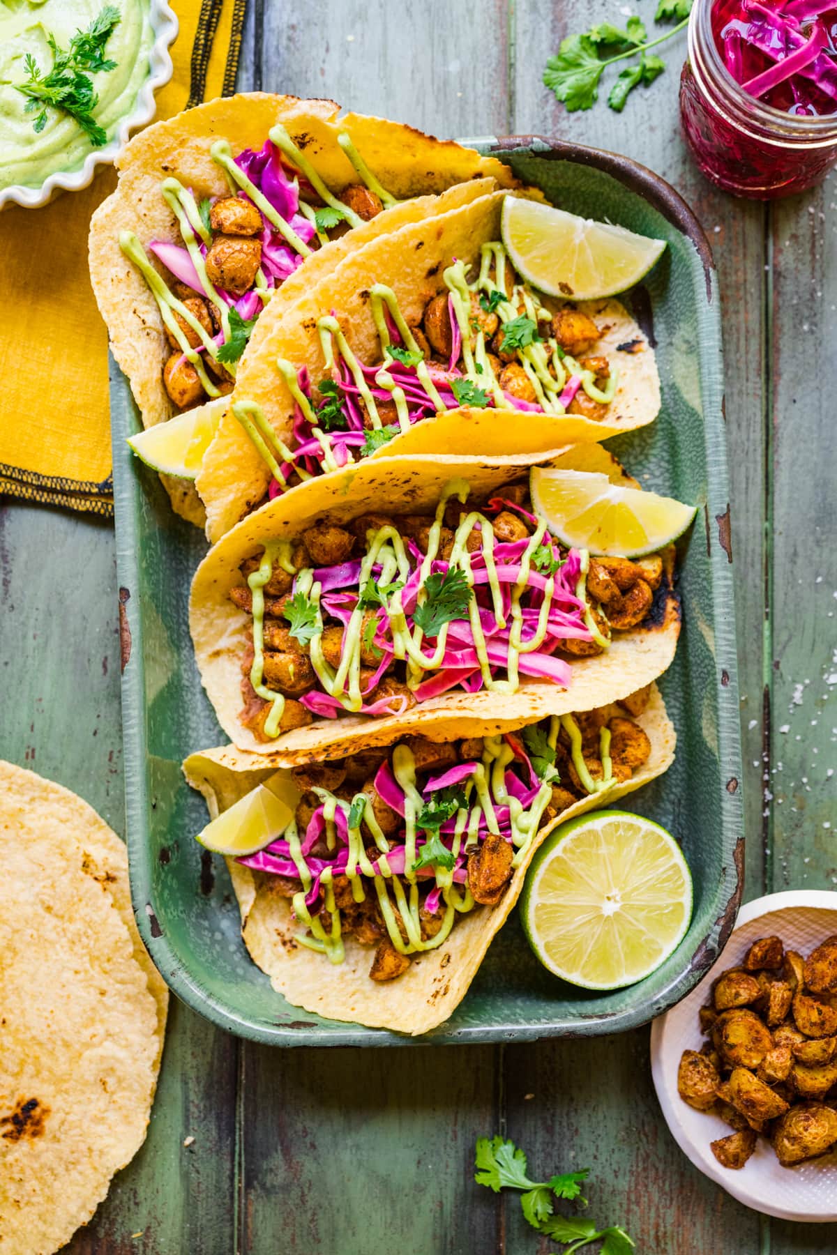 Finished potato tacos in green tray with a drizzle of cilantro and some pickled red cabbage.