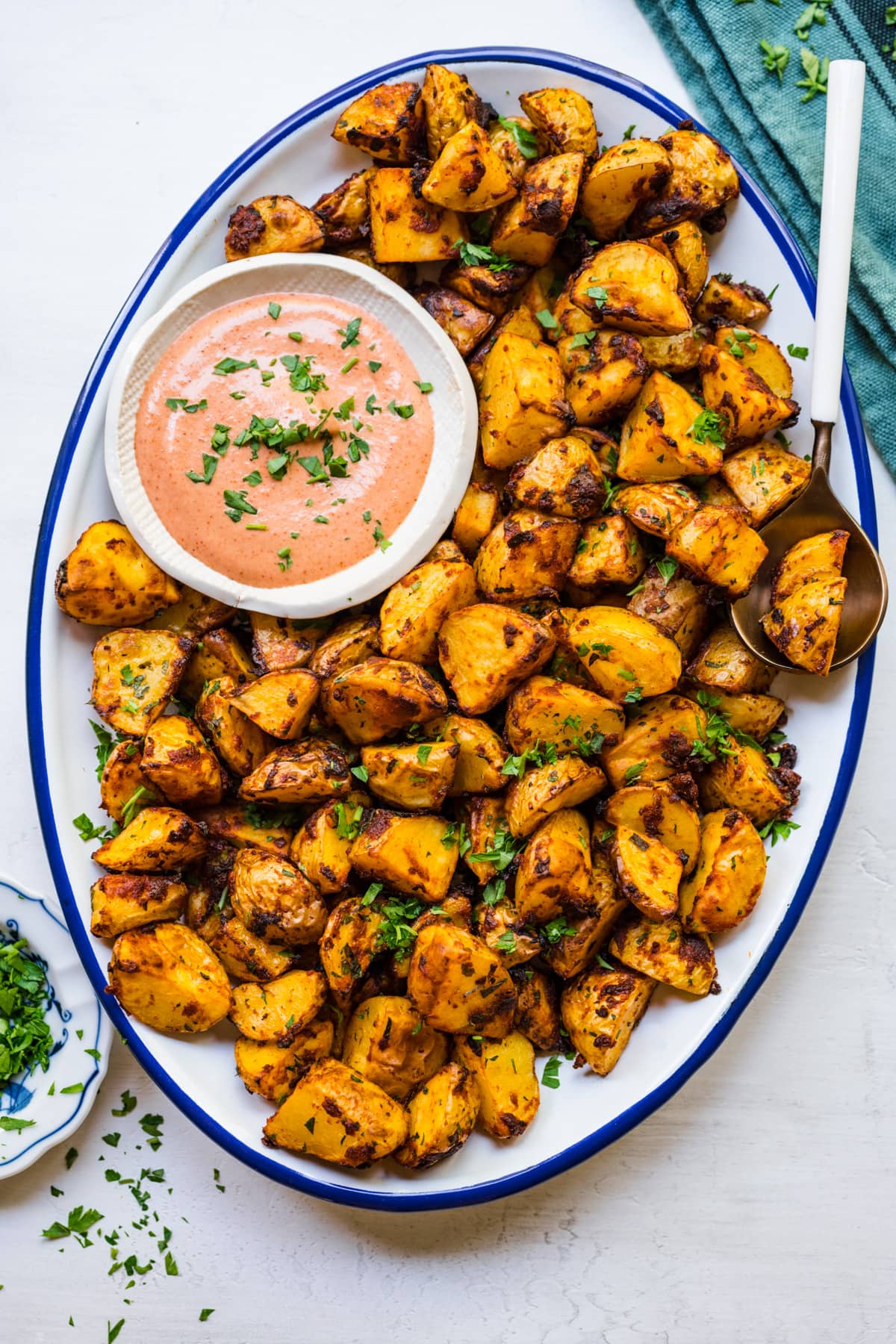 Finished Spanish potatoes on a white serving platter with dipping sauce.