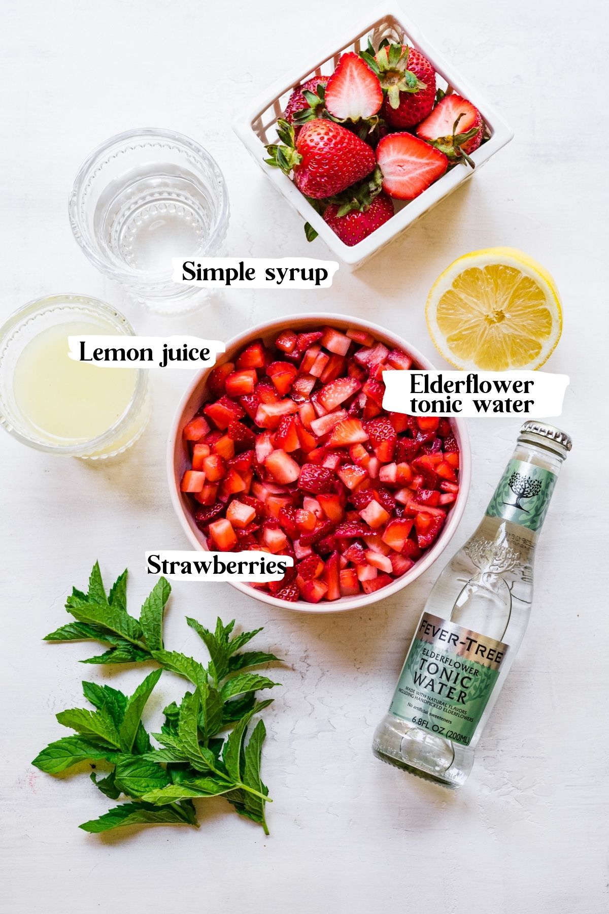 Overhead of strawberry mocktail ingredients including strawberries, lemon juice and elderflower tonic water.