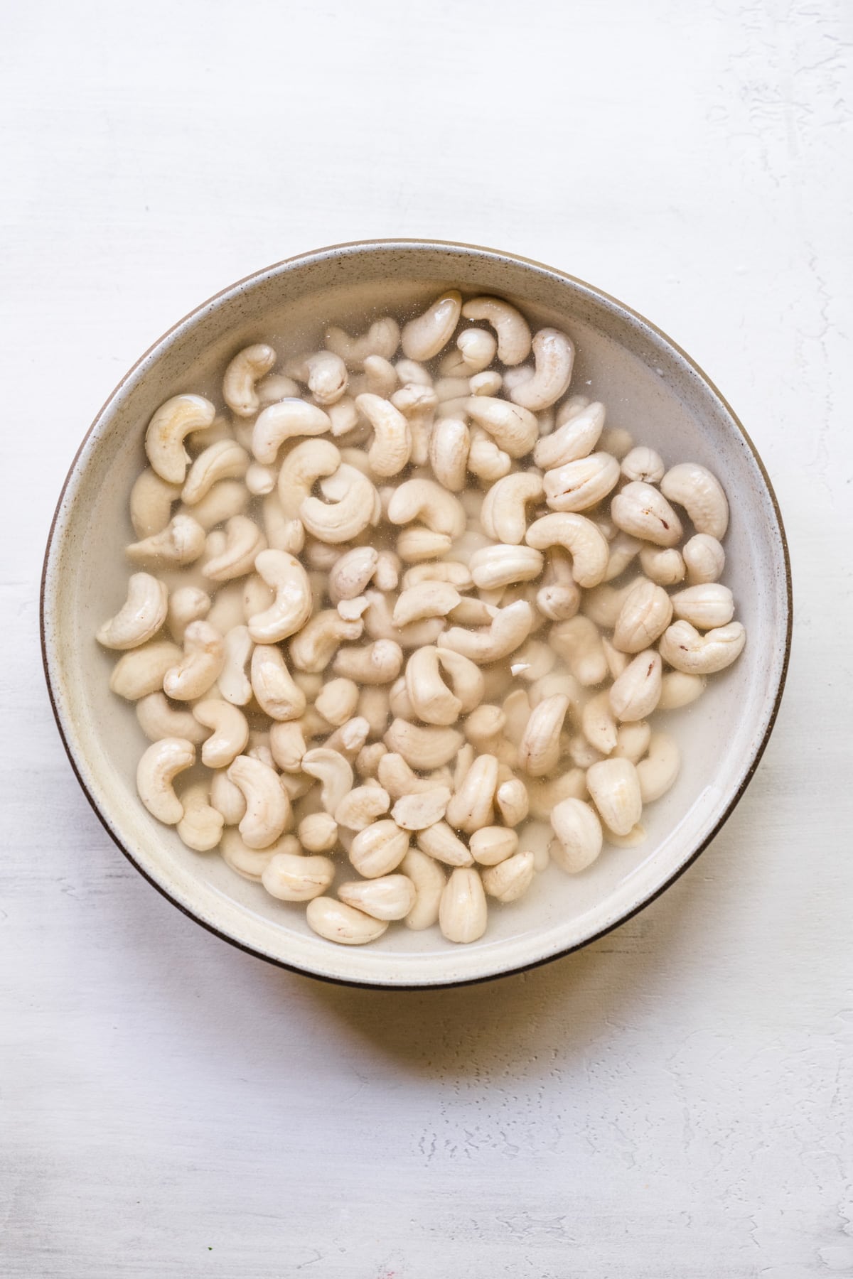 Overhead view of cashews soaking in water in a bowl.