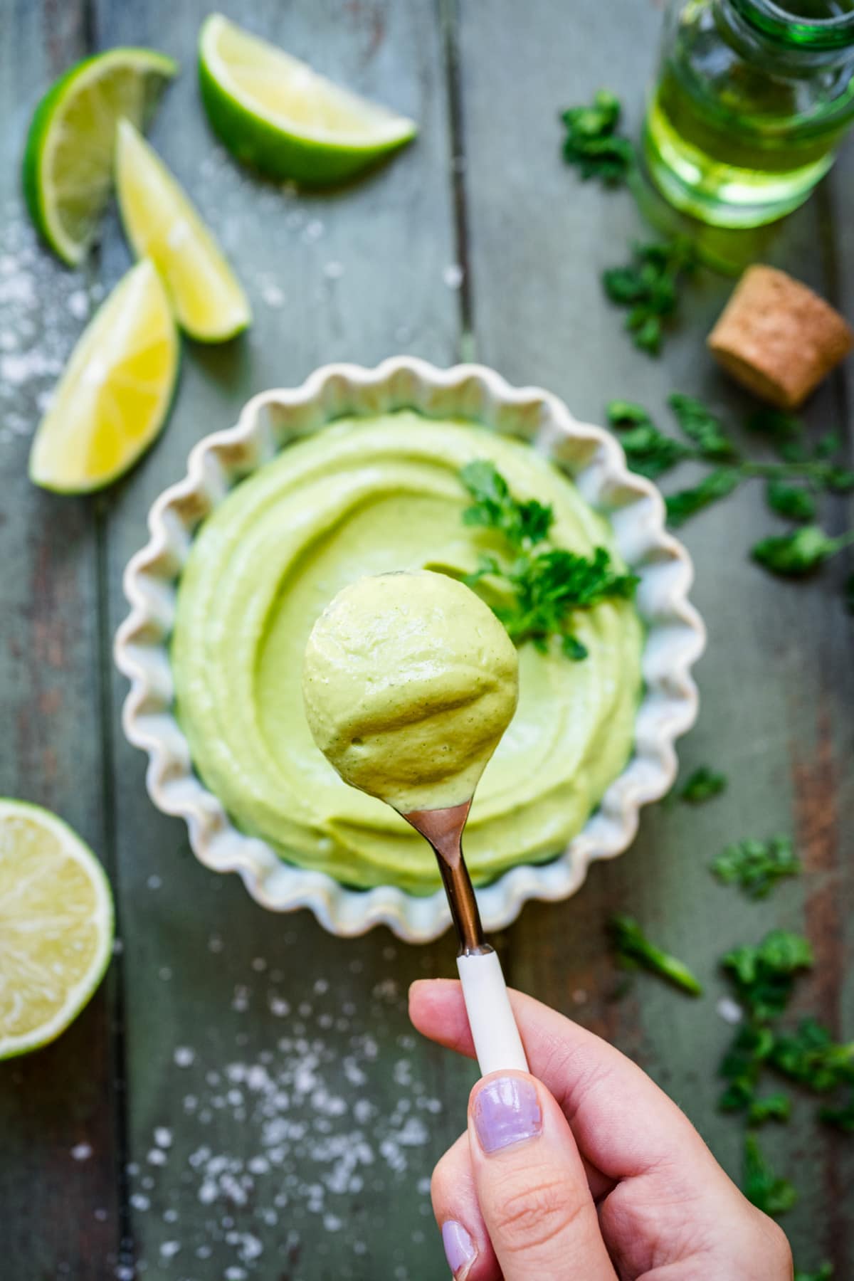 Overhead view of spoon of avocado crema held above a ramekin.