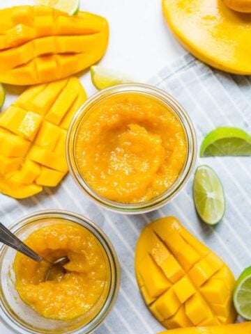 Finished mango jam in mason jar with mangos on the side.