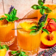 Close up view of peach bourbon smash in glass with basil and peach garnish.
