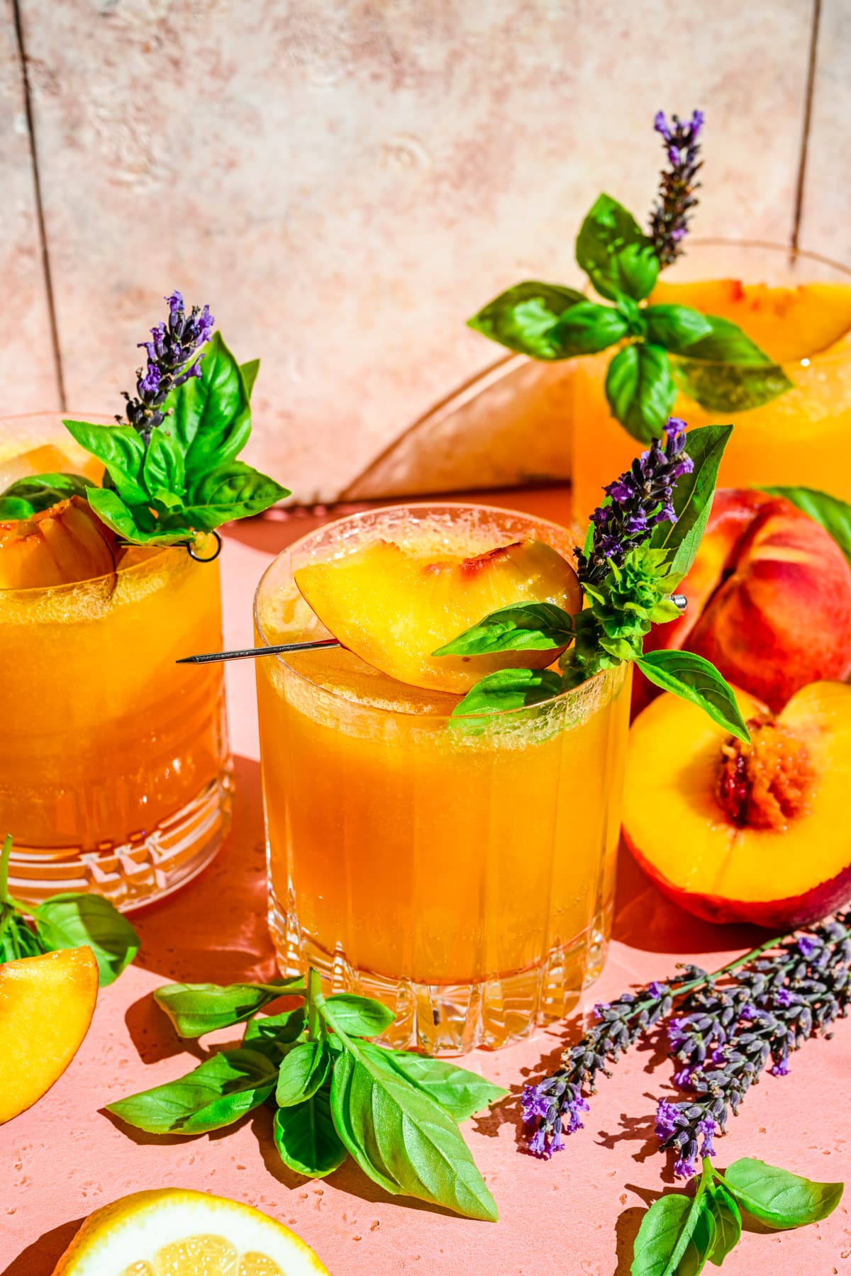 Close up view of peach bourbon smash in glass with basil and peach garnish. 