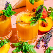 Close up view of peach bourbon smash in glass with basil and peach garnish.