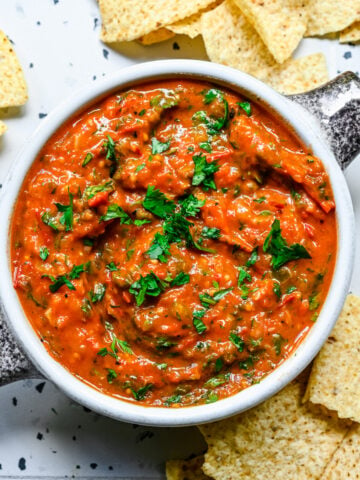 overhead view of cherry tomato salsa in a bowl with tortilla chips around it.