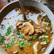 Close up of spoon with mushroom in it in the soup.