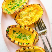 Overhead view of grilled spaghetti squash garnished with herbs.
