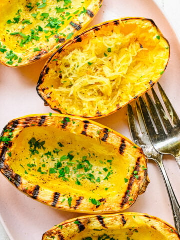 Overhead view of grilled spaghetti squash garnished with herbs.