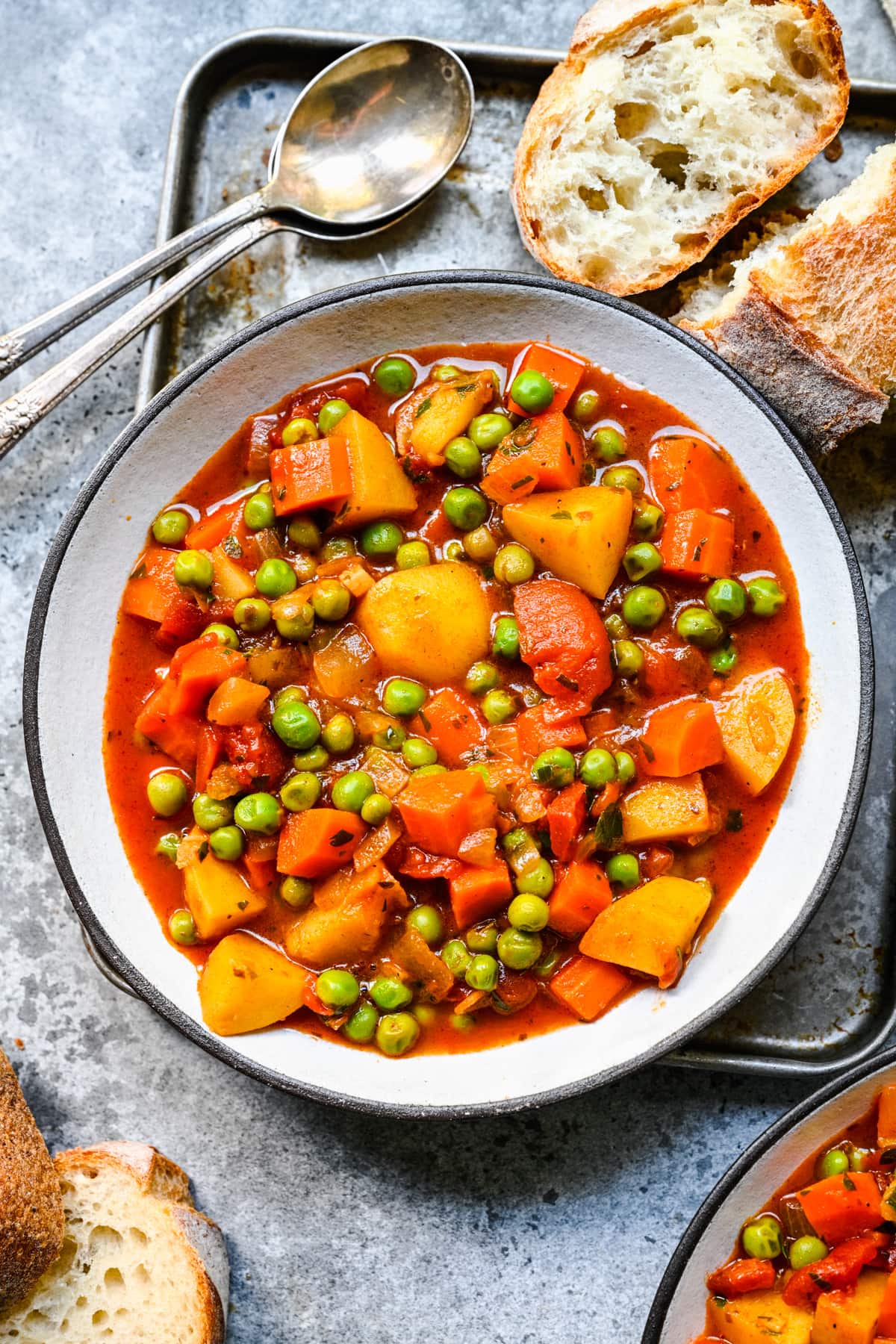 Overhead view of pea stew in a white bowl alongside bread.