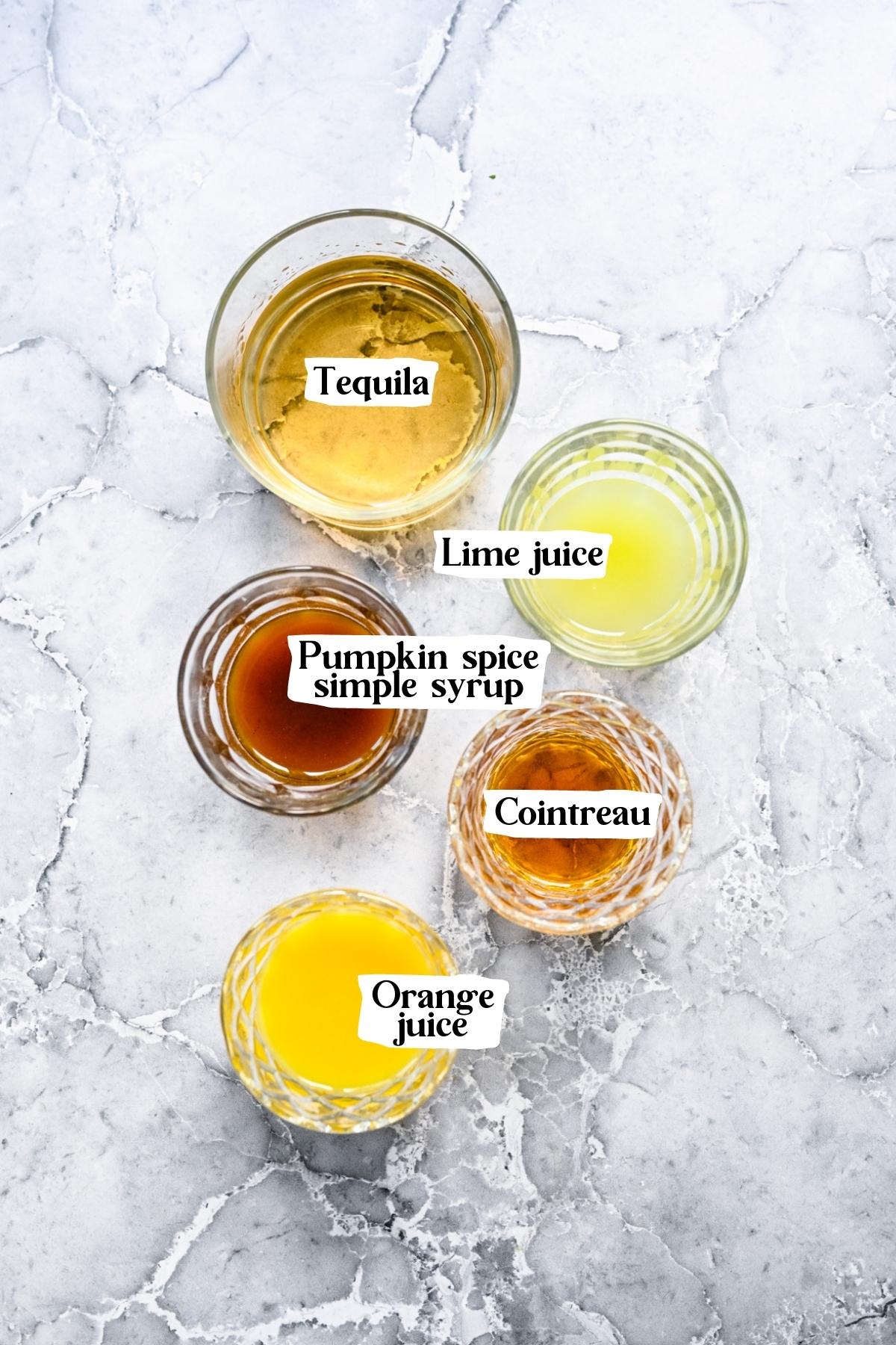 Overhead view of pumpkin spice margarita ingredients, including tequila, lime juice, and orange juice.