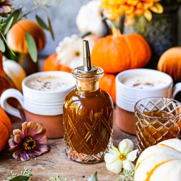 Pumpkin spice syrup with autumn decorations, pumpkins, flowers, and cozy fall vibe, perfect for seasonal fall recipes and drinks.