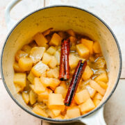 Overhead view of stewed pears in a pot with cinnamon sticks on top.