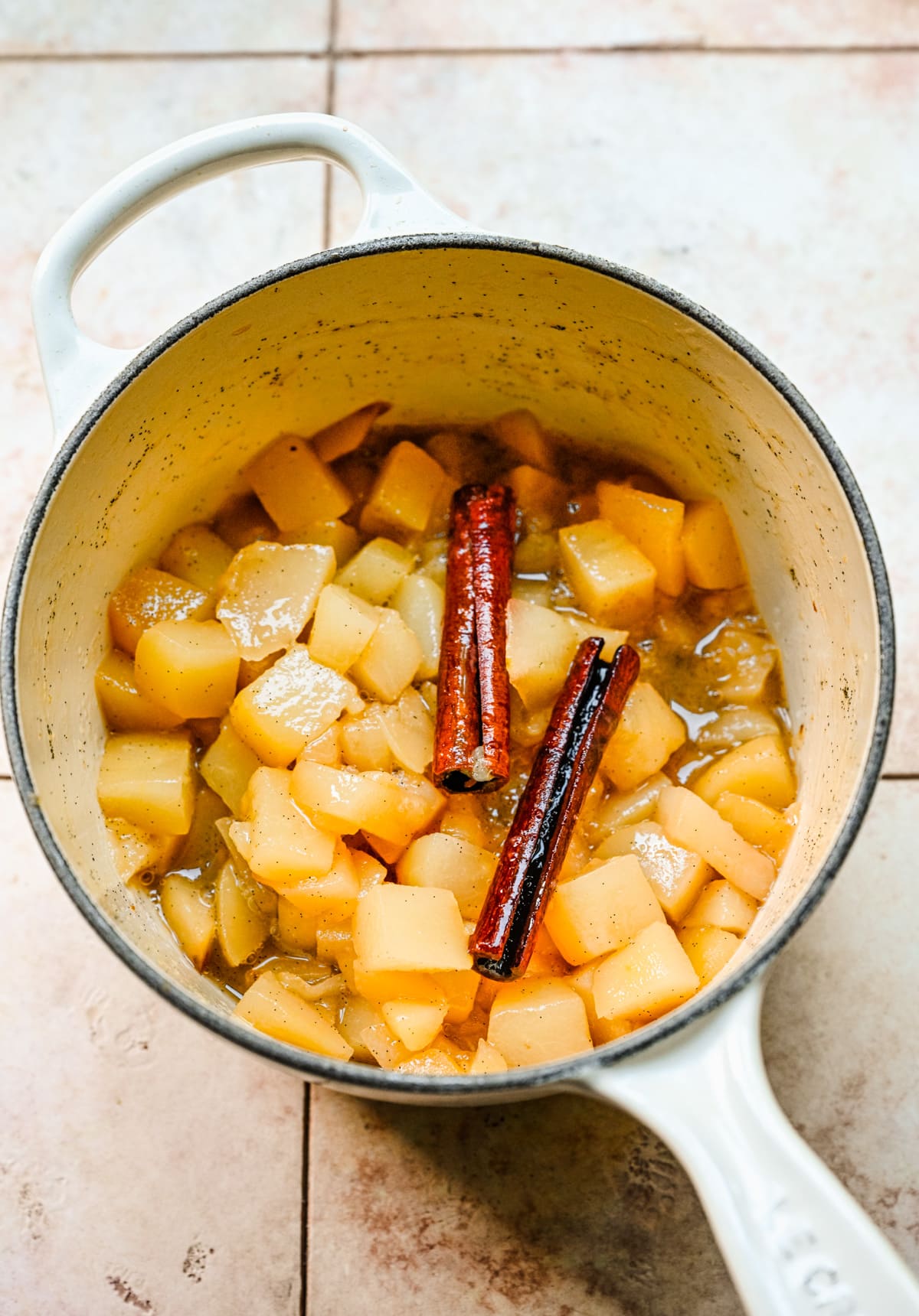 Overhead view of stewed pears in a pot with cinnamon sticks on top.