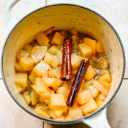 Overhead view of stewed pears in a pot with cinnamon sticks on top.