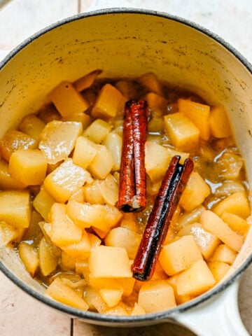 Overhead view of stewed pears in a pot with cinnamon sticks on top.