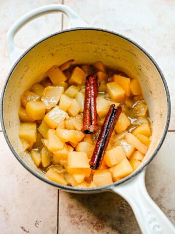 Overhead view of stewed pears in a pot with cinnamon sticks on top.