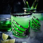 Close up view of poison apple green cocktail in skeleton hand glass.