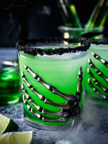 Close up view of poison apple green cocktail in skeleton hand glass.