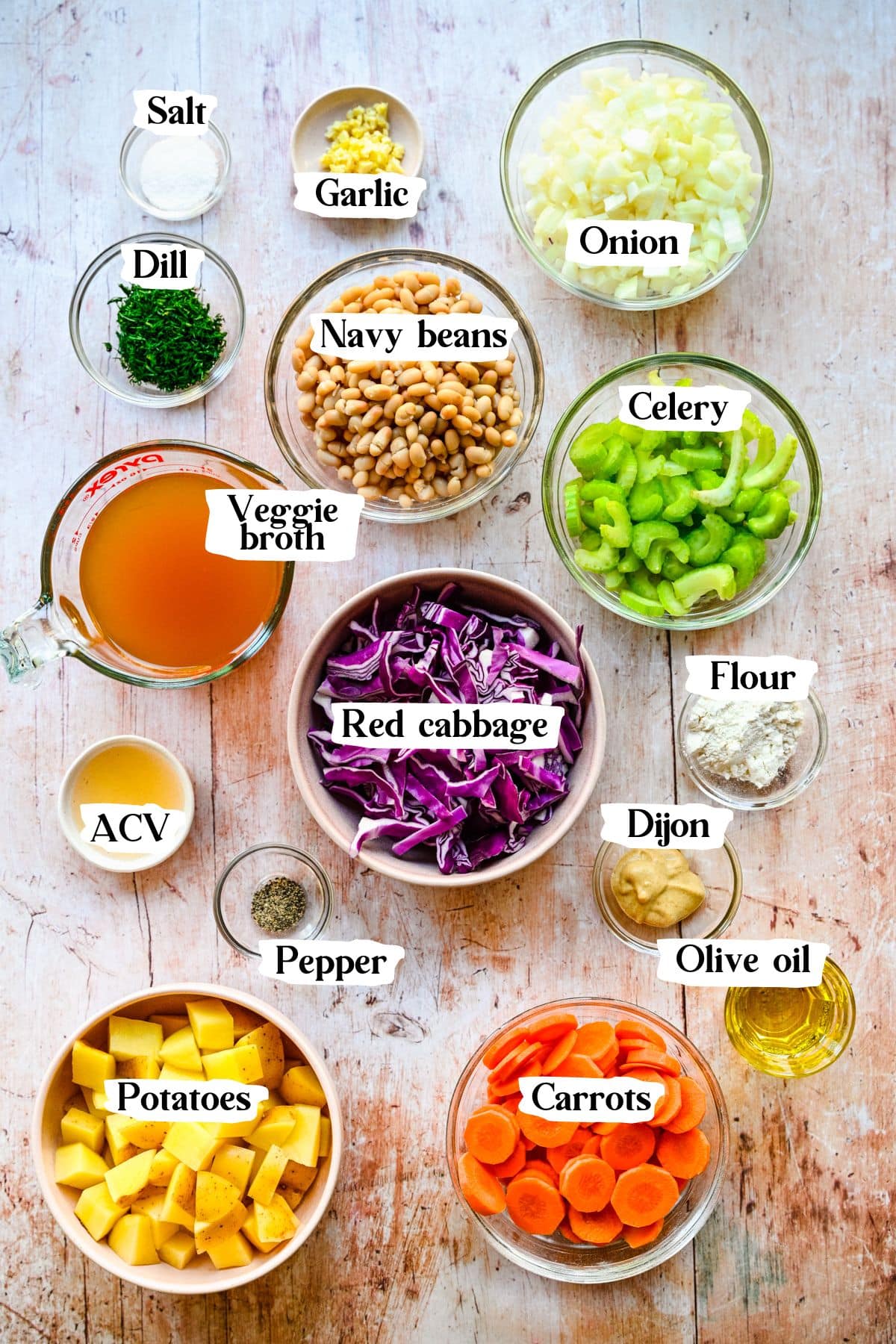 Red cabbage soup ingredients in glass bowls, including vegetables, broth, spices, herbs and beans.