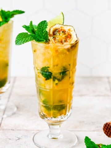 Passionfruit mojito in a tall glass with fruit and herb garnish.