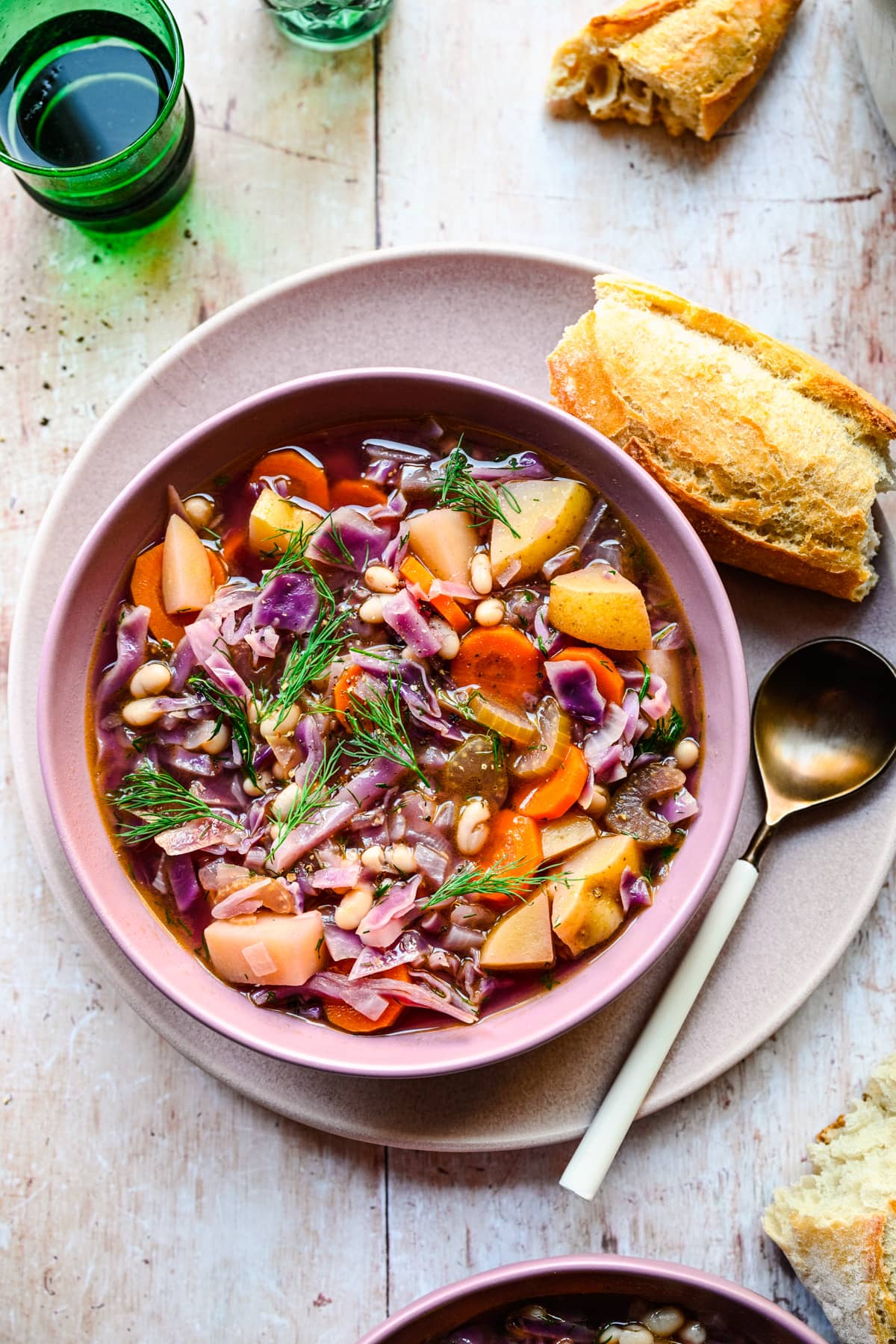 Finished red cabbage soup in a purple bowl served with bread.