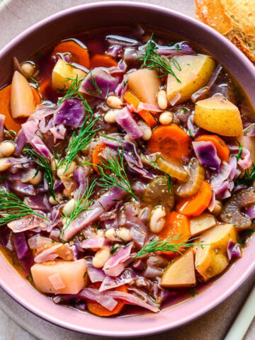 Close up of the finished red cabbage soup in a purple bowl.