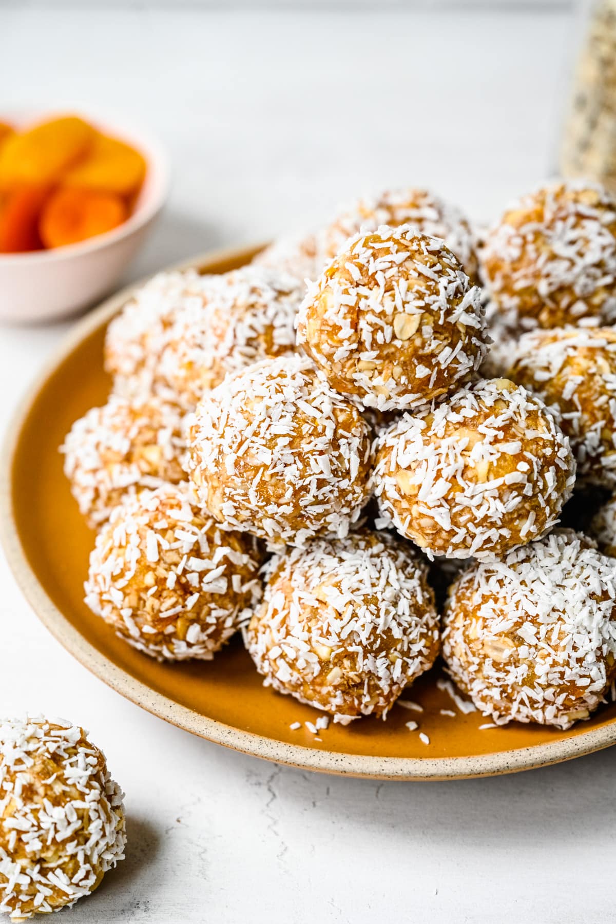Side view of apricot bliss balls stacked on a yellow plate.