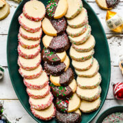 Overhead view of vegan butter cookies on a green platter with christmas ornaments.
