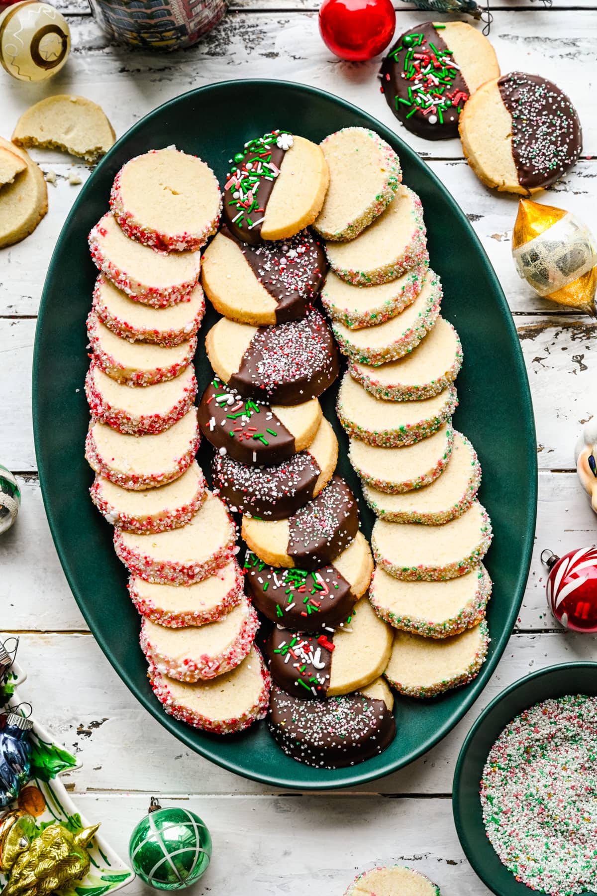 Overhead view of vegan butter cookies on a green platter with christmas ornaments.