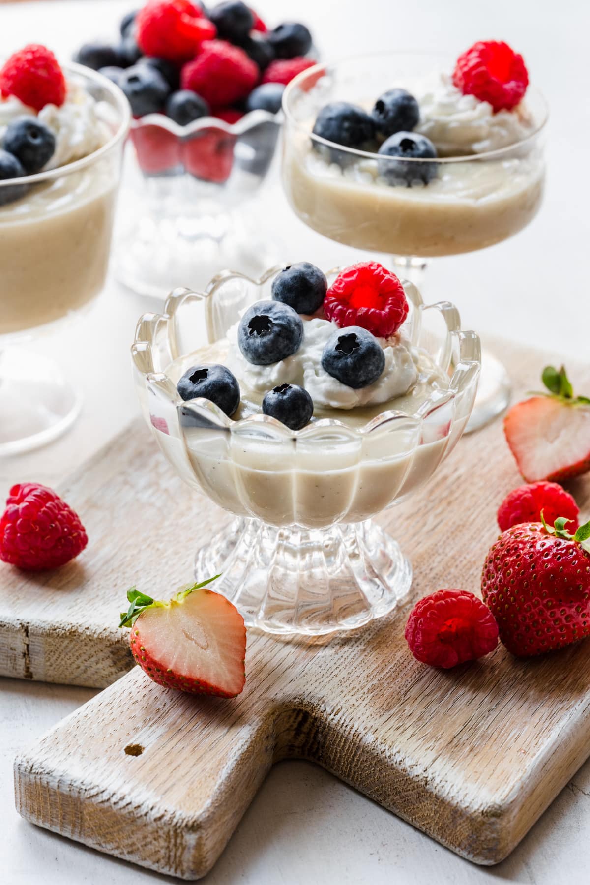 Finished vanilla pudding in glasses topped with berries and whipped cream.