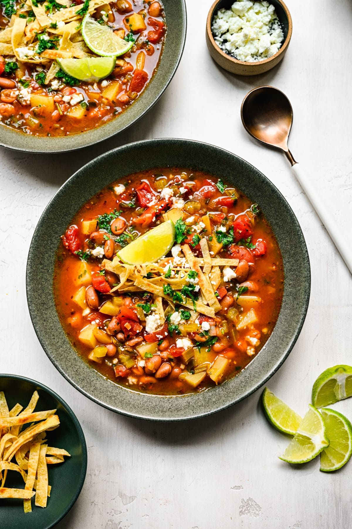 Overhead of the finished pinto bean soup with limes and tortilla strips on the side.