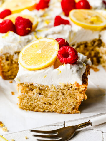 Finished slice of lemon cake with raspberries and lemon slice on top.