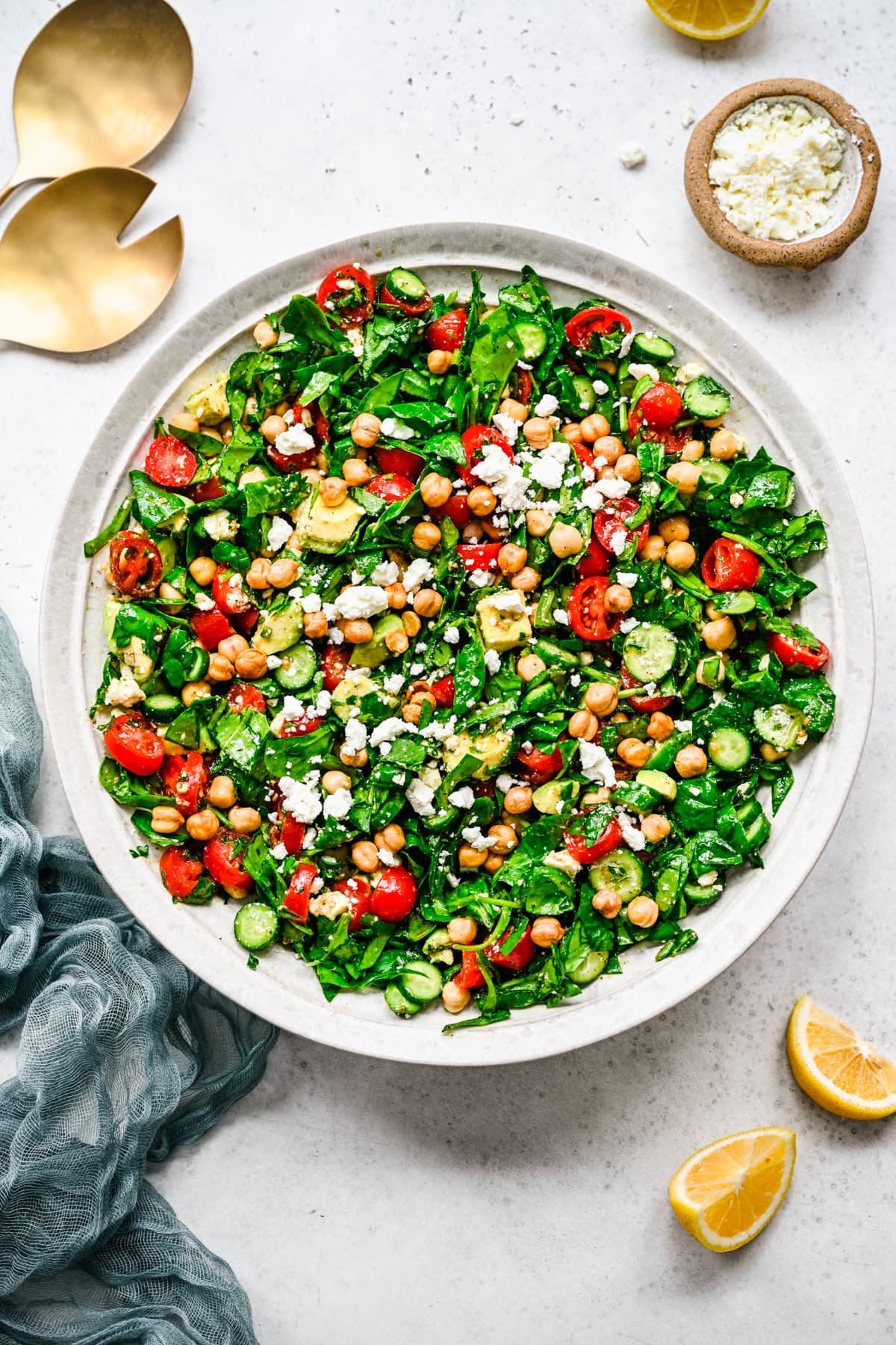 Overhead of the finished spinach chickpea salad in a white bowl with a linen and serving utensils.