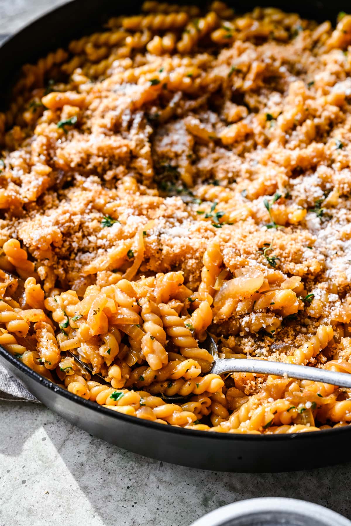 Close up view of french onion pasta in a large pot on serving spoon.