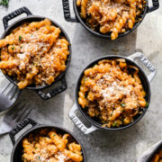 Four small cast iron cocottes filled with french onion pasta and topped with parmesan cheese.