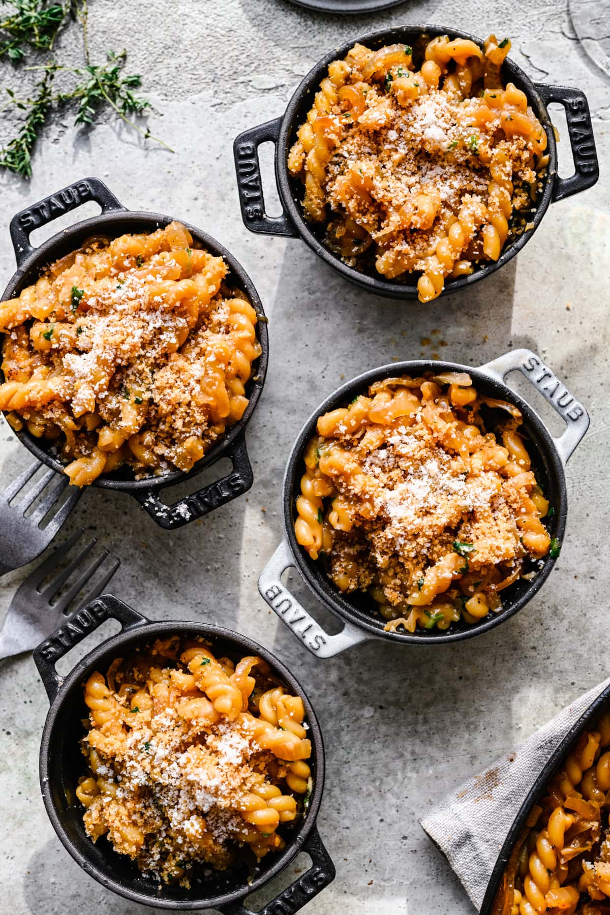 Four small cast iron cocottes filled with french onion pasta and topped with parmesan cheese. 